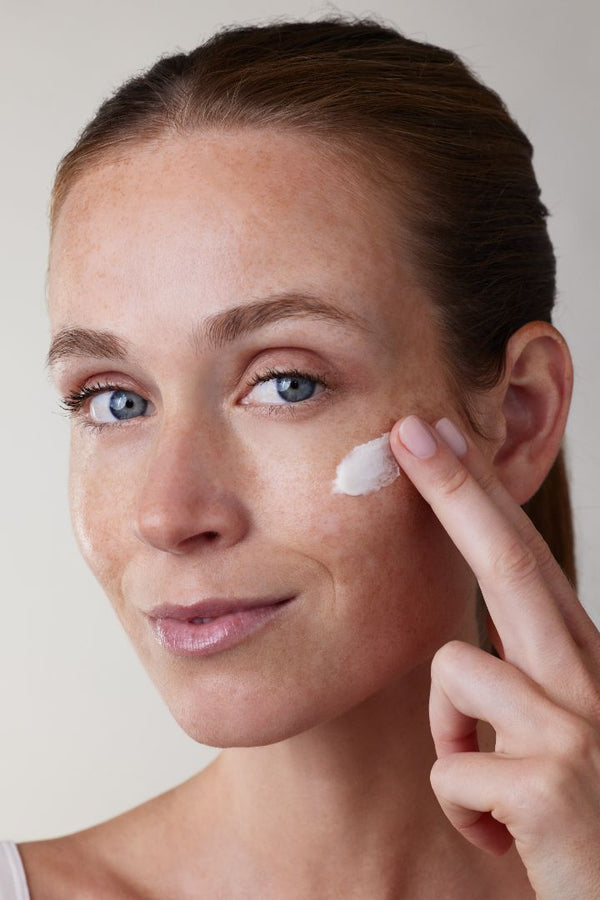 Portrait d’une femme appliquant une noisette de crème sur sa joue