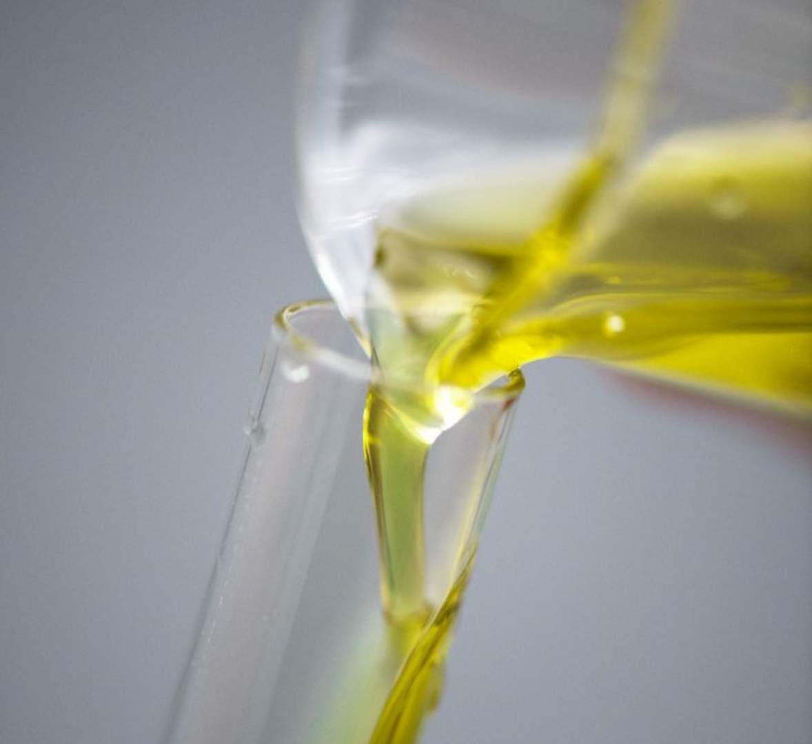 Éco-extrait huileux d’algue, de couleur jaune, en train d’être versé dans un tube en verre, photographié en gros plan